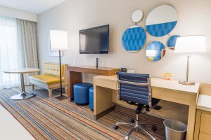 a hotel room with a desk, tv, table and bench