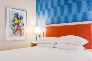 a hotel room pictured with a bed and Mickey Mouse picture on the wall
