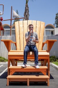 the General Manager of Howard Johnson Anaheim, Jonathan Whitehead, speaks into a microphone atop a giant orange beach chair