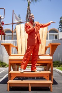 pop culture historian Charles Phoenix holds a microphone atop the large orange Adirondack chair at Howard Johnson Anaheim