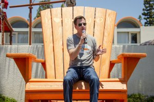 the General Manager of Howard Johnson Anaheim, Jonathan Whitehead, speaks into a microphone atop a giant orange beach chair