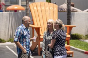 three adults talk at the Howard Johnson Anaheim retro re-do near the large orange Adirondack chair