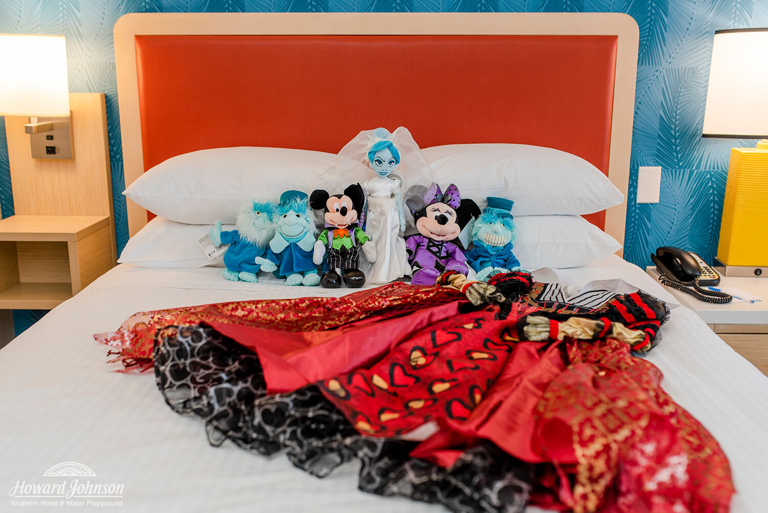 Stuffed Disney characters and a dress costume lay on a hotel room bed