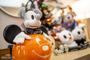a Halloween Mickey Mouse stuffed animal inside a Mickey pumpkin on a table next to Disney halloween decor