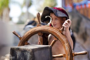 a little girl wearing a pirate hat with a gold hand hook mans the ship's wheel