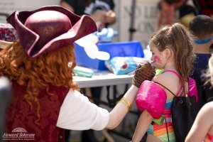 a woman dressed as a pirate paints on the face of a little girl