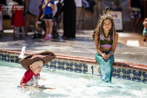 a little boy dressed as a pirate plays in the pool while a little girl dressed as a mermaid sits on the edge and smiles
