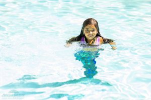 a little girl with a mermaid tail swims in the pool