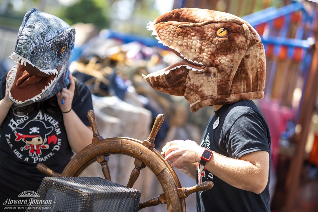 two men wear dinosaur heads over their heads