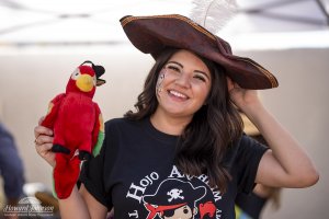 a woman smiles with a stuffed parrot and pirate hat on her head