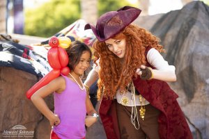 A little girl wearing an inflatable parrot on her shoulder poses for a picture with a woman in a pirate costume