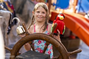 a little girl with a gold hand hook and parrot mans the ship's wheel at Castaway Cove