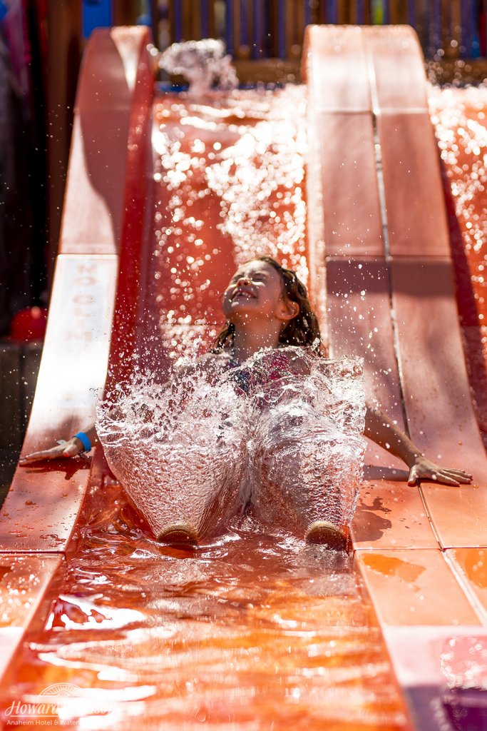 a little girl slides down a slide with splashing water