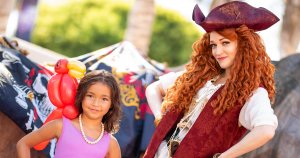 a woman dressed as a pirate poses with a little girl with an inflatable parrot on her shoulder