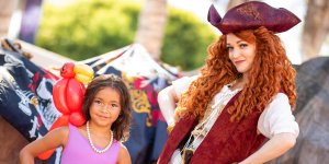 a woman dressed as a pirate poses with a little girl with an inflatable parrot on her shoulder