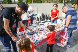 young children approach a craft table as volunteers watch on and assist as a parent takes a photo