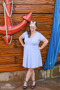 a woman in a blue dress wearing sunglasses poses for a picture near a red ship anchor