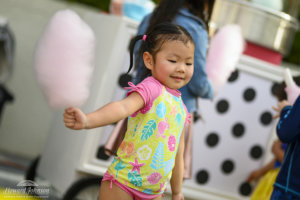 a little girl wearing a swimsuit holds pink cotton candy in her hand