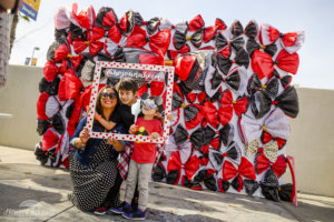 a woman and her two boys pose for a photo holding a wooden polka dot frame in front of a backdrop of polka dot bows