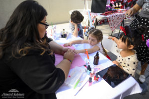 a woman paints the nails of a young girl while her friend watches at the table