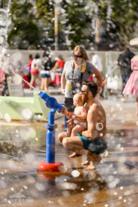 A man supports a baby in his lap while playing with a bubble shooter gun as a female watches on