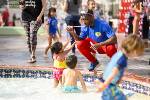 A man plays blows bubbles to two children in the pool