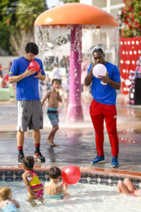 two men blow up balloons near a pool at Howard Johnson Anaheim hotel as children watch on and play in the pool