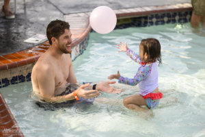 a man and a small girl play with a pink balloon in the air while in the pool
