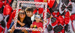 A woman and two boys pose for a picture with a wooden pokadot picture frame with the @hojoanaheim social media handle on it