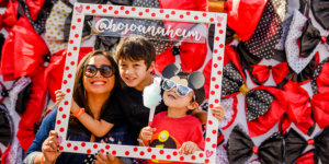 A woman and two boys pose for a picture with a wooden pokadot picture frame with the @hojoanaheim social media handle on it