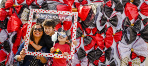 A woman and two boys pose for a picture with a wooden pokadot picture frame with the @hojoanaheim social media handle on it