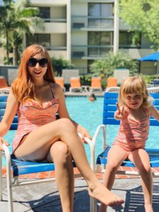 A woman and little girl are pictured in swimsuits sitting in chairs by the pool