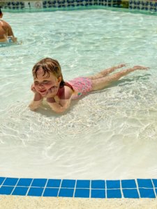 A little girl is pictured laying on her stomach in the shallow end of the pool with her head in her hands